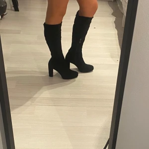 Svarta stövletter från Tamaris - Säljer ett par snygga svarta stövletter från Tamaris. De är knähöga med en rejäl klack som ger en elegant look. Perfekta för höst och vinter, och de passar både till fest de har en tight passform 