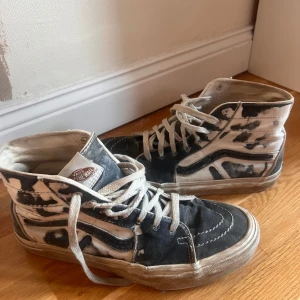 Svartvita sneakers från Vans - Säljer ett par coola svartblåa Vans sneakers i välanvänt skick. De har en unik mönsterdesign med snörning och högre skaft. Perfekta för en avslappnad streetwear-look!