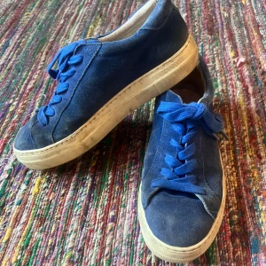 Blå sneakers i mocka - Säljer ett par blå sneakers i mocka med vita sulor. Skorna har blå snörning och är i välanvänt skick. Perfekta för hösten