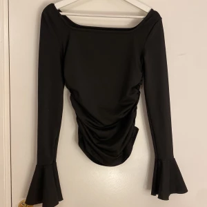 Svart långärmad topp med volangärmar - Elegant svart topp med långa ärmar och volangdetaljer vid ärmsluten. Perfekt för en stilren look. Passar för storlek xs och s! Har aldrig använt den.