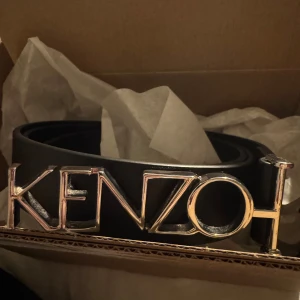 Kenzo bälte - Säljer detta snygga svarta bältet från Kenzo. Perfekt för att ge en stilren touch till din outfit. Bältet har en klassisk design som passar till många olika stilar. passar från xxs-m! Aldrig använt💕 Nypris ca 2000kr