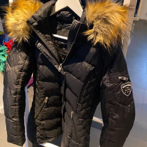 Svart dunjacka med pälsdetaljer - Snygg svart dunjacka från rockandblue  med pälsdetaljer på huvan. Har andvänt jackan typ 10 gånger och inte sen mer för jag inte gillar den. Perfekt för vintern/kalla dagar.