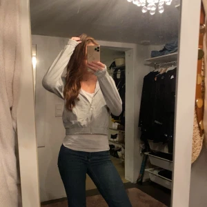 Grå hoodie - Säljer en stilren grå hoodie med dragkedja framtill. Perfekt för en avslappnad look. Den har långa ärmar och en bekväm passform.