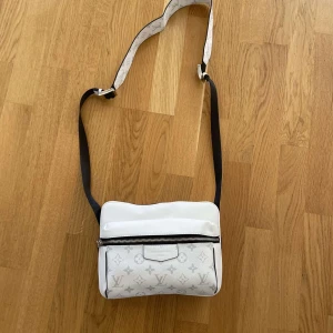 Vit axelväska med monogram - Snygg vit axelväska med monogrammönster och justerbar axelrem. Väskan har en dragkedja framtill och är perfekt för att bära med sig det nödvändigaste. Stilren design som passar till många olika outfits.