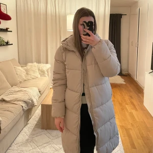 Beige lång dunjacka med huva - Säljer en beige lång dunjacka med huva. Säljer på grund av att den inte kommer till användning. Prislapp kvar, nypris 349kr.