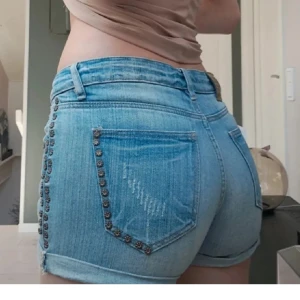 Blå jeansshorts med nitar - Snygga blå jeansshorts med coola nitar längs fickorna. De har en lågmidjad passform och klassisk femficksdesign. Perfekta för en avslappnad sommarlook!