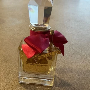 Viva la juicy parfym - Elegant parfymflaska med en kristalliknande kork och en dekorativ röd rosett runt halsen. Flaskan har en gyllene etikett och en charm i form av en nyckel. Perfekt för den som älskar lyxiga detaljer den är nästan ny testad två gånger .