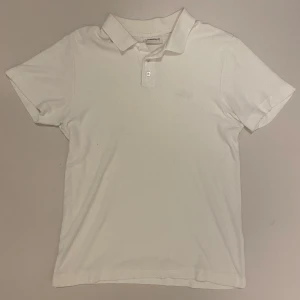 Vit frotté pikétröja från Lindbergh - Snygg vit frotté pikétröja från Lindbergh med klassisk krage och knappslå. Perfekt för en stilren look. Broderad logga på bröstet ger en extra touch. En knapp saknas längst upp men inget som märks när den är på, skriv vid minsta fråga eller fundering🔥👍