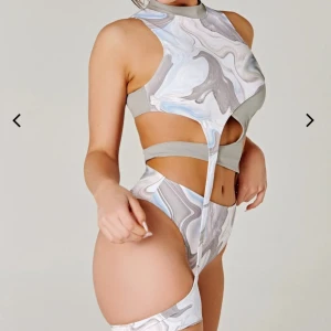 Mönstrad gartier topp - Unik ärmlös topp med abstrakt mönster i beige, grå och blå toner. Toppen har en asymmetrisk design med cut-out detaljer och hög hals samt höfthållare. Perfekt för dans eller när du vill sticka ut. Säljer tillhörande trosor. Garderobsrensning så kika gärna på övriga auktioner.