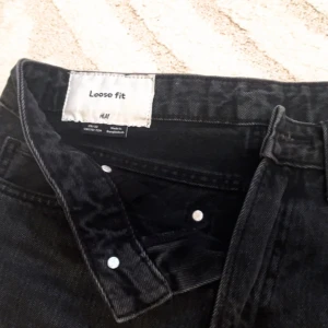 Svarta loose fit jeans från H&M - Säljer ett par svarta loose fit jeans från H&M. De har en klassisk design med fem fickor och knappgylf. Perfekta för en avslappnad stil.