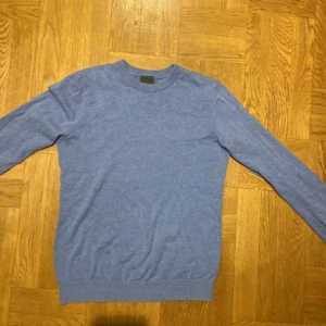 Blå tröja från H&M - Säljer en stilren blå tröja från H&M i slim fit. Tröjan har långa ärmar och en rund halsringning med ribbade kanter. Perfekt för en avslappnad look.