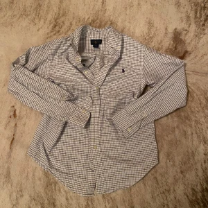Rutig skjorta från Ralph Lauren - Snygg rutig skjorta från Ralph Lauren i blått och vitt. Skjortan har långa ärmar och klassiska knappar framtill. Perfekt för en stilren look.