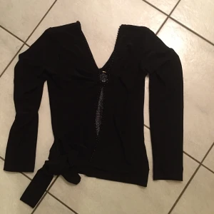 Svart långärmad topp med knyt - Snygg svart långärmad tröja med v-ringning och knyt i midjan. Perfekt för en stilren look. Passar bra till både jeans och kjol.