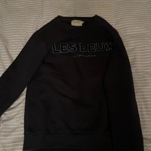 Svart sweatshirt från Les Deux - Säljer en stilren svart sweatshirt från Les Deux med logga på framsidan. Tröjan har långa ärmar och en rund halsringning. Loggan har mjuk päls. Bra skick också. Storlek S