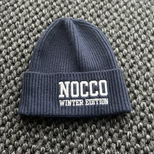 Mörkblå stickad mössa från NOCCO - Snygg mörkblå stickad mössa från NOCCO med texten 'Winter Edition' broderad framtill. Perfekt för kalla dagar. Mössan är marinblå 
