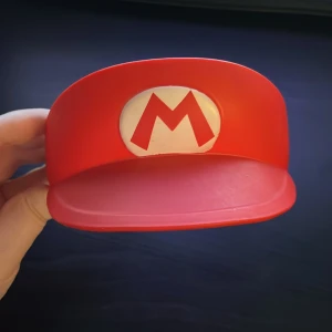 Super Mario Diadem - Här har vi ett Mario Diadem från McDonald’s 2015 kollaboration med Nintendo! Det är i barn storlek, men kan säkert vara en bra present om man har ett yngre syskon eller liknande. Ändarna är lite böjda från dålig förvaring och materialet får lätt ”fläckar” (se bild 3)