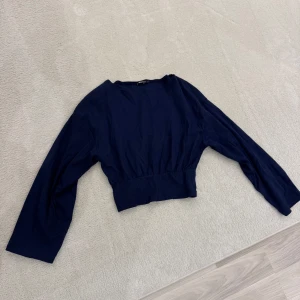 Mörkblå topp från Gina Tricot - Snygg mörkblå topp från Gina Tricot med långa ärmar och en croppad design. Perfekt för en stilren look. Oanvänd. 