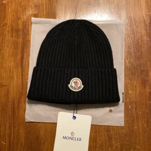 mössa från Moncler - Snygg svart ribbad mössa från Moncler med broderad logotyp framtill. Perfekt för att hålla värmen under kyliga dagar. Stilren design som passar till det mesta.