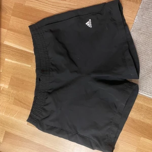 Svarta shorts från Adidas - Snygga svarta shorts från Adidas med elastisk midja och logga på framsidan. Perfekta för träning eller en avslappnad dag.