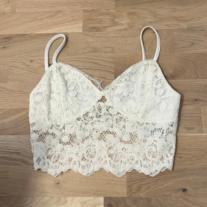 Vit spetslinne från NLY Trend - Säljer en söt vit spetslinne från NLY Trend i storlek XS. Linnet har smala axelband och ett vackert blommigt spetsmönster. Perfekt för varma sommardagar eller som ett lager under en kavaj.