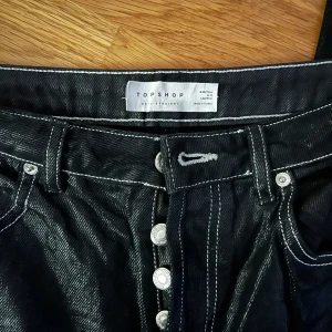 Svarta jeans från Topshop - Snygga svarta jeans från Topshop med hög midja och raka ben. De har en klassisk femficksdesign och knappar framtill. Perfekta för en stilren look.