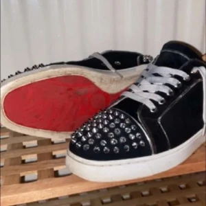 Svarta sneakers med nitar från Christian Louboutin - Snygga svarta sneakers från Christian Louboutin med silverfärgade nitar på tån och sidorna. Skorna har en vit sula och klassisk röd undersida. Perfekta för att ge en edgy touch till din stil.