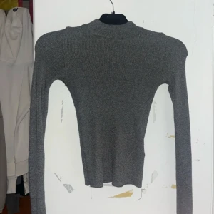 Grå ribbad polotröja från Gina Tricot - Säljer en stilren grå ribbad polotröja från Gina Tricot. Tröjan har en tight passform och långa ärmar, perfekt för kyligare dagar. Den är både bekväm och snygg, ett måste i garderoben!