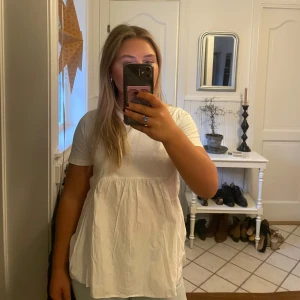 Vit blus med volang framtill - Säljer en söt vit blus med korta ärmar, samt en volang/rynkat detalj nedanför bysten. Detaljen ger genast en festligare look. 