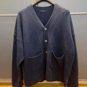 Mörkblå kofta från Paul & Friends - Säljer en stilren mörkblå kofta från Paul & Friends. Koftan har en v-ringad design med knappar framtill och praktiska fickor. Endast använd 1 gång så skicket är 10/10. Hör av er vid eventuella frågor!🤝 