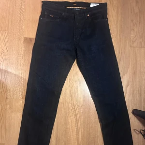 Mörkblå jeans från Boss - Snygga mörkblå jeans från Boss i modellen 'Maine BC-L-P'. De har en klassisk femficksdesign och en regular passform. Perfekta för en stilren look. HELT NYA. Nypris är 1099