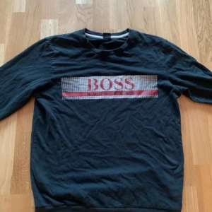 Hugo Boss  - Snygg marinblå tröja från Boss med ett stort logotryck i rött och vitt på bröstet. Perfekt för en casual look med långa ärmar.