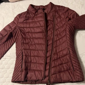 Vinröd quiltad jacka - Snygg vinröd quiltad jacka med dragkedja och hög krage. Perfekt för kyligare dagar med sin stilrena design och bekväma passform.