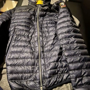 Svart quiltad jacka från Parajumpers - Säljer en svart quiltad jacka från Parajumpers med dragkedja och hög krage. Jackan har en broderad logga på ärmen och är perfekt för kyligare dagar. Den är lätt och smidig att bära. Strl M skriv gärna om ni har frågor eller liknande.