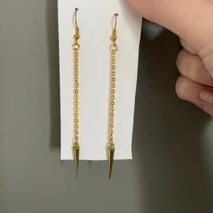 Guldörhängen med kedja och spets - Snygga och trendiga guldörhängen med lång kedja och spetsig detalj. Perfekta för att ge en edgy touch till din outfit. Lätta att bära och passar till många olika stilar. Edblad dupeee!!