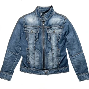 Blå jeansjacka med dragkedja - Snygg blå jeansjacka med dragkedja och ståkrage. Jackan har två bröstfickor med knappar och en stilren design. Perfekt för en casual look.