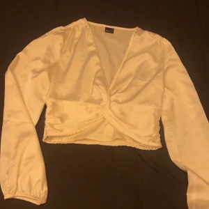 Gräddvit omlottopp - Snygg typ gräddvit omlottopp med långa ärmar och v-ringning. Toppen har en elegant omlottdesign framtill och elastisk midja baktill för en bekväm passform. Perfekt för en stilren look.