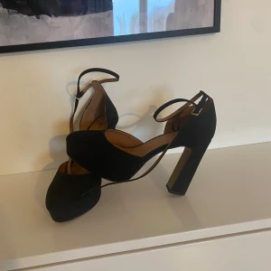 Svarta klackskor med ankelrem - Eleganta svarta klackskor med ankelrem och hög klack. Perfekta för en stilren look. Skorna har en rundad tå och justerbar rem för bästa passform.