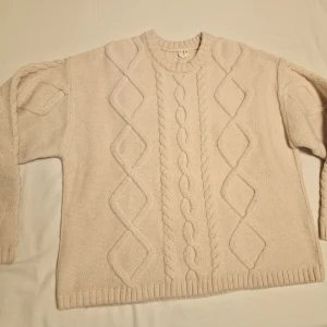 Beige stickad tröja oversize - Mysig beige stickad tröja i dtorlex XS med kabelstickat mönster. Oversize. Perfekt för kyliga dagar med sin klassiska design och ribbade kanter.