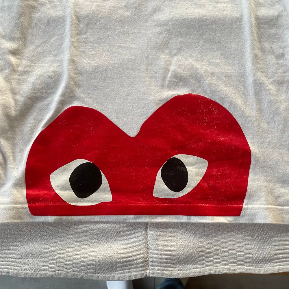 säljer en snygg vit t-shirt från Comme des Garçons med det ikoniska röda hjärtat med ögon på bröstet och en stor röd grafik längst ner. Strl S. Skick 8,5/10. Passar till alla tillfällen!. T-shirts.