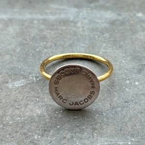 Marc Jacobs ring - Säljer min marc jacobs ring för att jag ej använder den. Den är äkta och köpt på sellpy. Fint skick!! Plattan uppe på ringen är silver och ringen runt fingret är i guld. Passar perfekt till mina marc jacobs öronhängen jag säljer!!🩷☺️