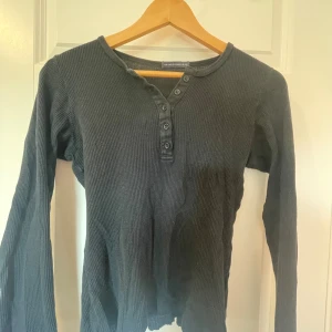 Svart ribbad tröja från Brandy Melville - Säljer en svart ribbad tröja från Brandy Melville. Den har långa ärmar och knappar framtill, vilket ger en snygg och avslappnad look. Perfekt för höst och vinter!