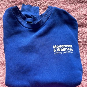 Blå sweatshirt med tryck - Säljer en snygg blå sweatshirt med tryck 'Movement & Wellness Active Lifestyle' på framsidan. Tröjan är perfekt för en aktiv livsstil och har en skön passform. Den är i bra skick och passar perfekt för både vardag och träning.
