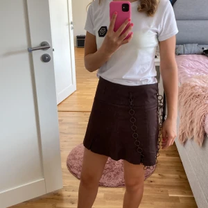 Brun kjol med kedjedetalj - Säljer en snygg brun kjol med en cool kedjedetalj på sidan. Kjolen är kort och har en stilren design som passar perfekt för både vardag och fest. Den är gjord i ett mjukt material och kommer med ett svart bälte för extra stilpoäng. Perfekt för höst och vår! kedjan går att ta bort lätt och skärpet ingår (från zara)