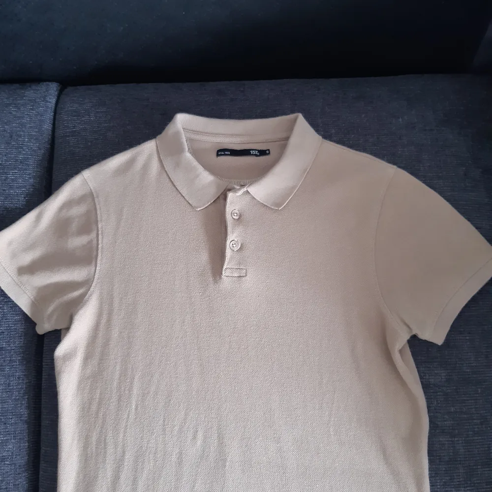 Säljer en stilren beige pikétröja från 157. Den har en klassisk krage och tre knappar framtill. Perfekt för en avslappnad men ändå snygg look. Passar bra till både vardag och lite finare tillfällen. Fint skick!!. T-shirts.