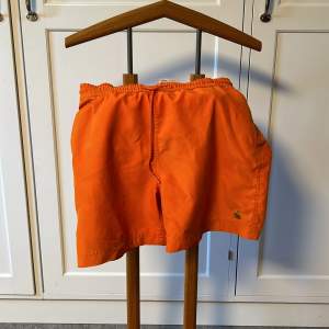 Säljer ett par snygga orange badshorts från Carhartt. Shortsen är i nyskick och redo för stranden eller poolen. 🏖️