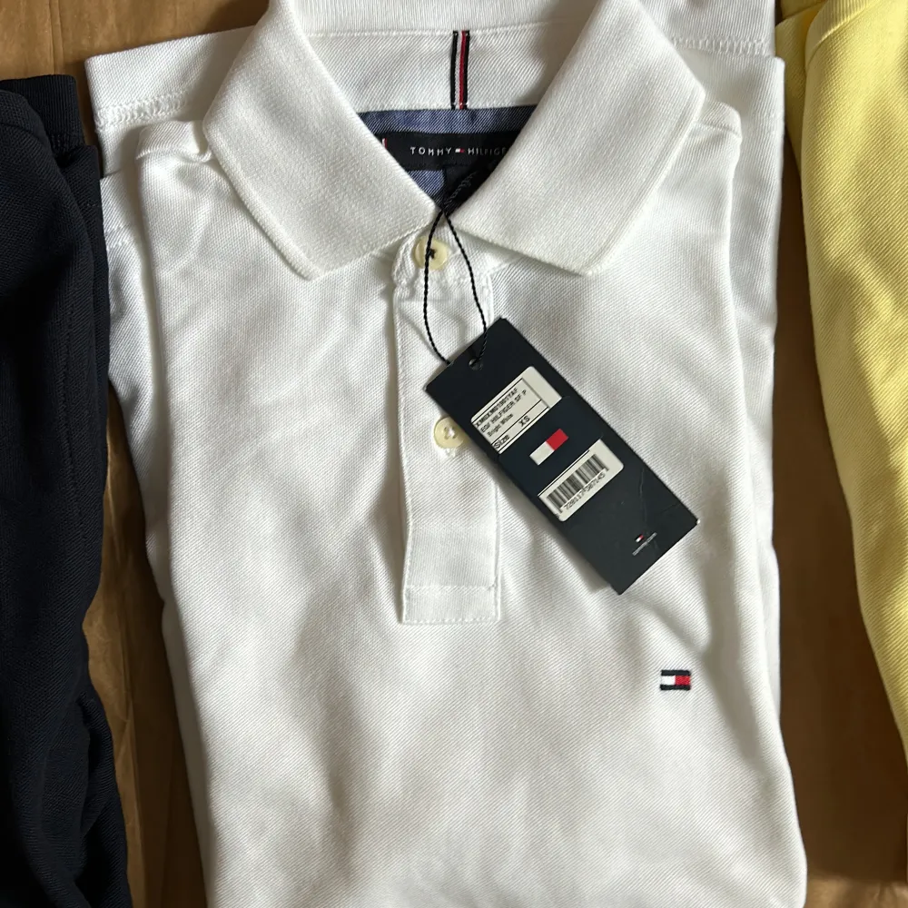 Säljer tre snygga pikétröjor från Tommy Hilfiger i olika färger: marinblå, vit och gul. Perfekta för både vardag och fest! De har en klassisk design med krage och knappar framtill. Märkets ikoniska logga syns diskret på bröstet.. Tröjor & Koftor.