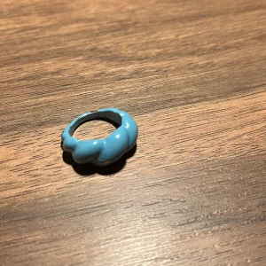 Blå ring med flätad design - En unik blå ring med en flätad design. Perfekt för att ge en färgklick till din outfit. Ringen har en slät yta och en modern look.