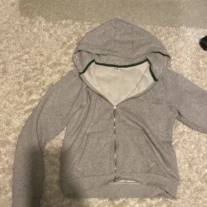 Grå hoodie från Lacoste - Säljer en grå hoodie från märket Lacoste. Dragkedjan är lite böjd och en pytte liten fläck som inte syns men annars toppskick. Köpt för ett tag sen från kidsbrandstore. Kan vara liten i storlek.