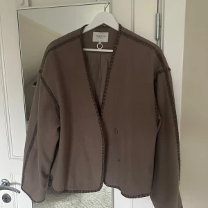Brun jacka från STOCKH LM studio  - Snygg brun jacka från STOCKH LM studio med dekorativa sömmar. Den har en öppen design med knappar och långa ärmar. Perfekt för en stilren look. Knappt använd❣️