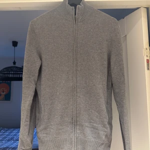 Grå full zip från Pier One - Snygg och stilren grå full zip från Pier One med dragkedja framtill. Perfekt för lager-på-lager under kyligare dagar. Tröjan är sparsamt använd och har inga defekter. 